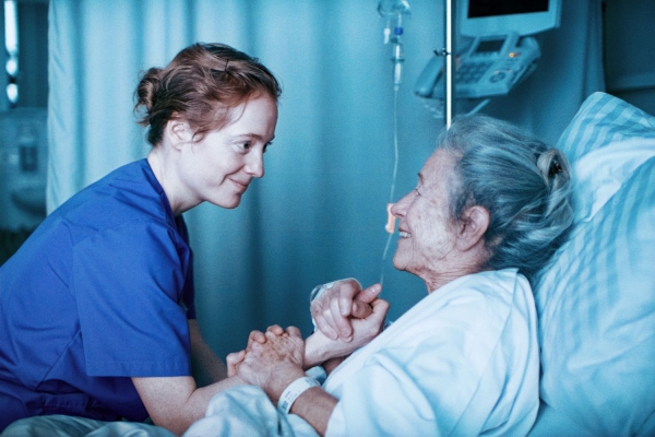 Kino: Heldin Bild: Floria sitzt an einem Krankenbett und hält die Hand einer älteren Frau.