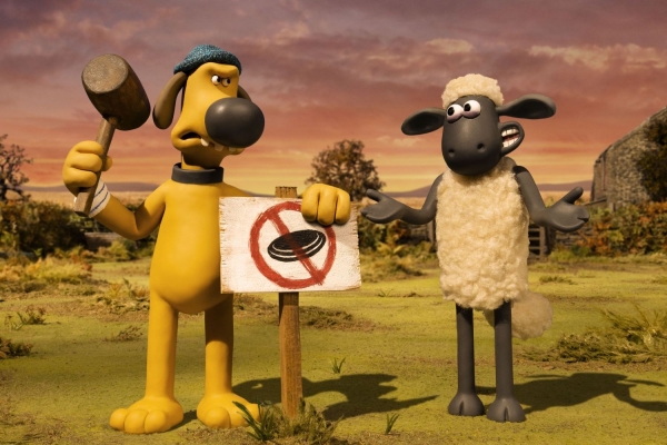 Shaun das Schaf Bild: Shaun (rechts) steht neben einem Hund, der ein Schild in den Boden rammt.