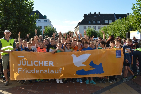 Jülicher Friedenslauf Bild: Die Teilnehmerinnen und Teilnehmer stehen hinter einem Banner mit der Aufschrift