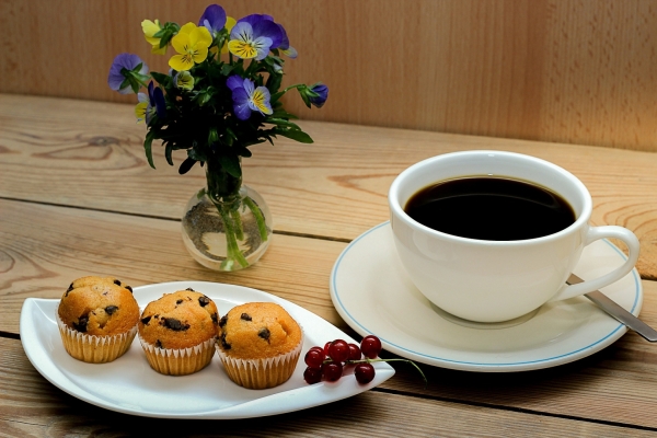 Bild: Kaffe und Kuchen stehen mit einer Blumenvase auf einem Tisch.