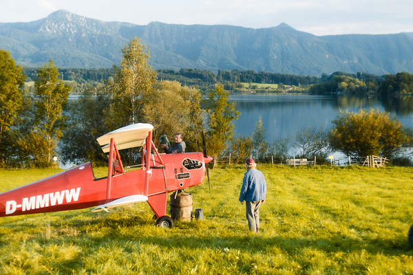 Bild: Ein rotes Propeller-Flugzeug steht auf einer Wiese und wird von einem Mann betankt.