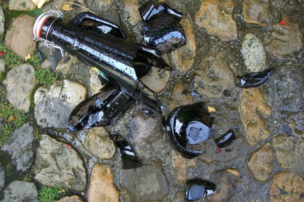 Bild: Eine zerbrochene Bierflasche auf einem gepflasterten Weg.