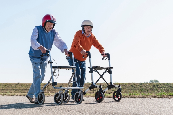 Bild: Zwei Senioren mit Helm laufen am Rollator einen Weg entlang