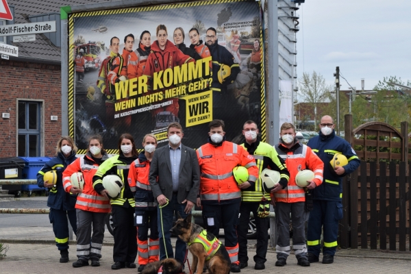 Wer kommt Bild: Vertrerer der verschiedenen HIlfs- und Rettungsdienst vor einem großen Plakat mit der Aufschrfit: Wer kommt, wenn nichts mehr geht? Die Katastrophenschützer*innen. Wenn nicht WIR, wer dann?