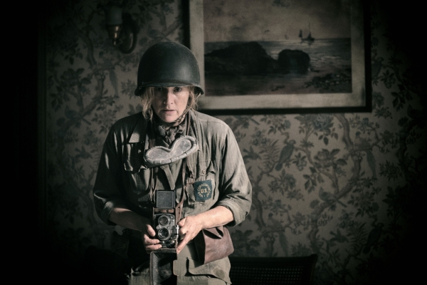 Kino: Die Fotografin Bild: Die Fotografin steht in einer Soldatenuniform in einem Raum und macht Fotos