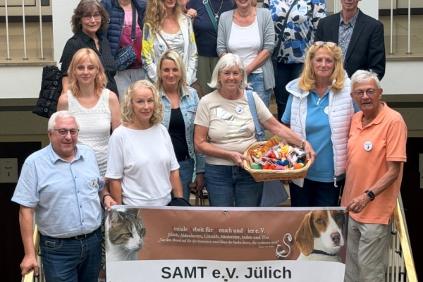 15 Menschen stehen auf einer Treppe, halten ein Banner vom SAMT e.V. Jülich