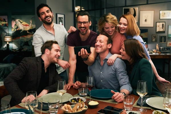 Das perfekte Geheimnis Bild: Drei Frau und vier Männer stehen und sitzen lachend um einen gedeckten Tisch