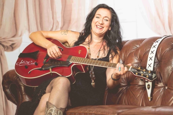 Bild: Jolina Carl sitzt mit einer Gitarre im Arm auf einem Sofa.