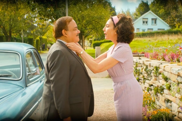 Bild: Hélène (r) richtet ihrem Mann Michel das Hemd. Beide stehen neben dem Auto auf der Straße.