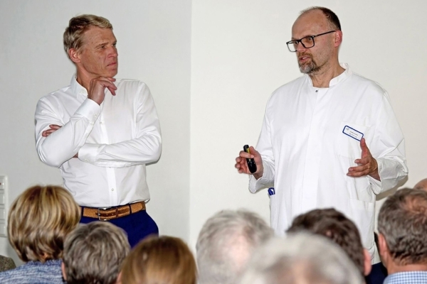 Zwei Ärzte  stehen vor dem sitzenden Publikum